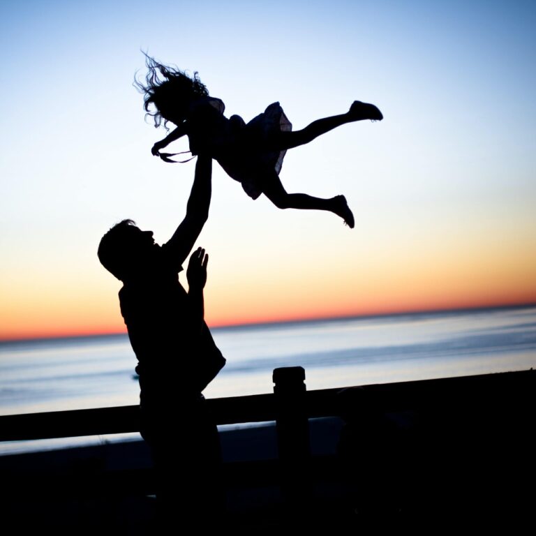 Silhouette of an adult lifting a child in the air at sunset by the ocean, capturing a moment as timeless and essential as understanding legal wills for future security.